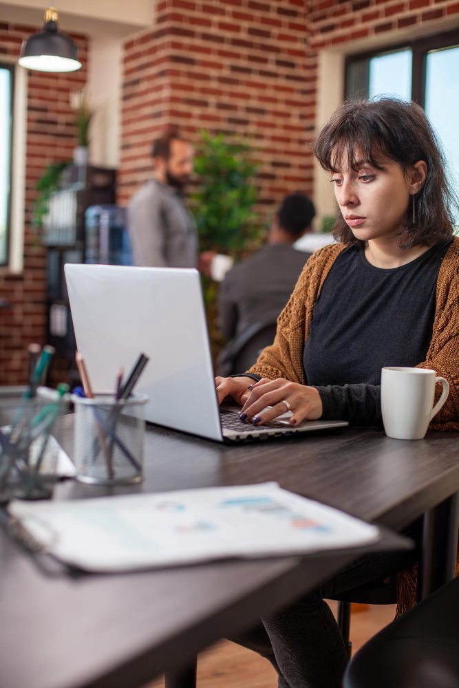Website design - woman working at a laptop in a brick-walled cafe