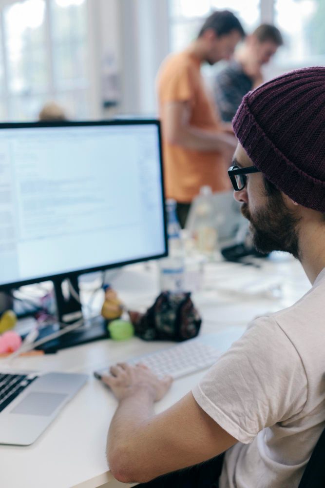 Website design - designer in a beanie working at a desktop in a busy studio