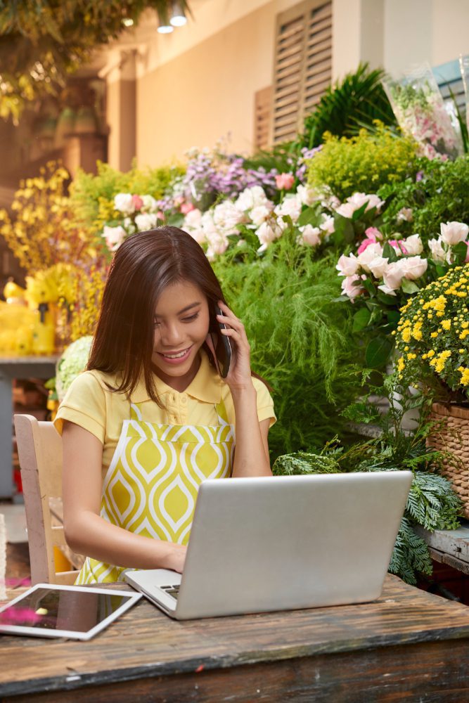 Ecommerce websites - florist taking a phone order at a laptop surrounded by flowers