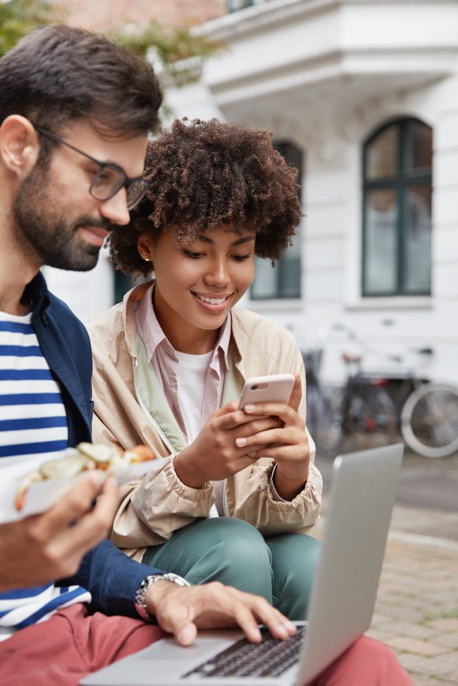 Website design - two people looking at a phone together outdoors with a laptop open