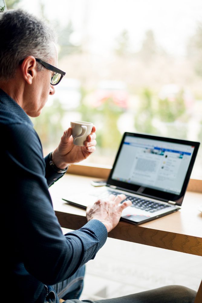 Man reviewing a website on a laptop by a window with a coffee