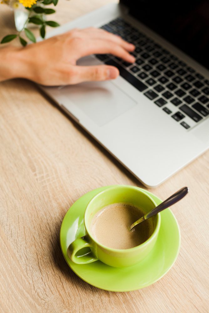 Web hosting - hand on a laptop trackpad beside a green cup of tea