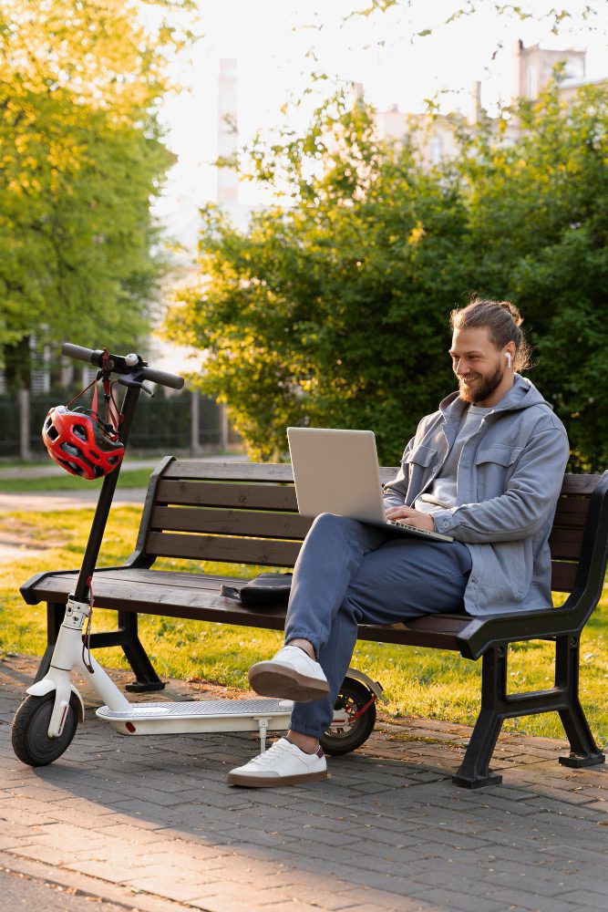 Website design - man working on a laptop on a park bench beside an e-scooter