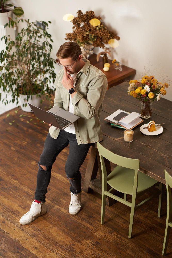 Website design - man using a laptop standing at a bench in a plant-filled cafe