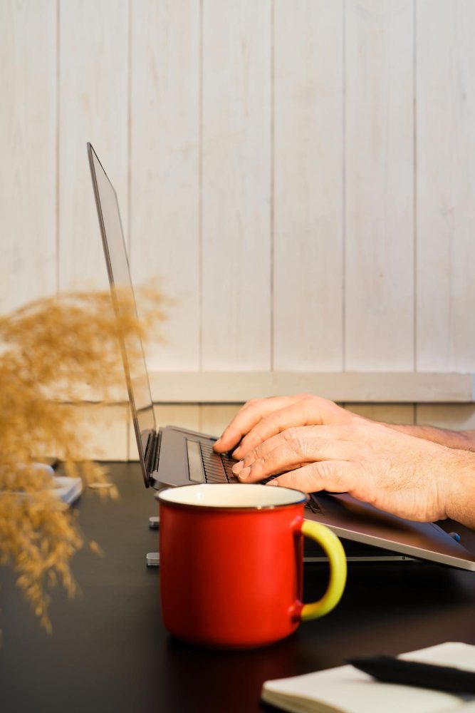 Website design - hands at a laptop beside a red enamel mug