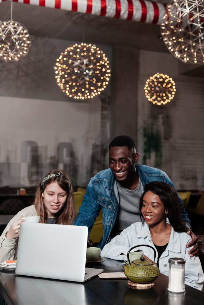 Website design - three friends looking at a laptop in a festively lit cafe