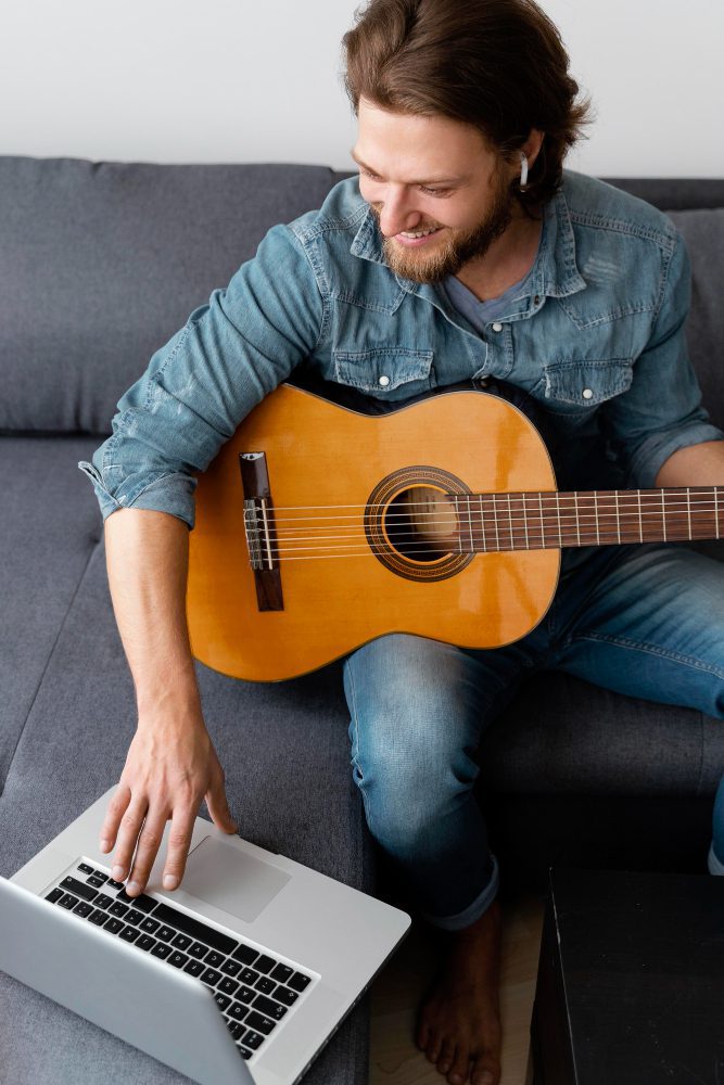 Website design - man playing an acoustic guitar beside an open laptop