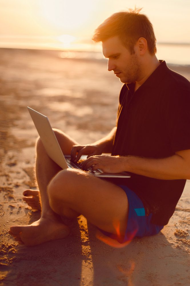 Website design - man using a laptop on a beach at sunset
