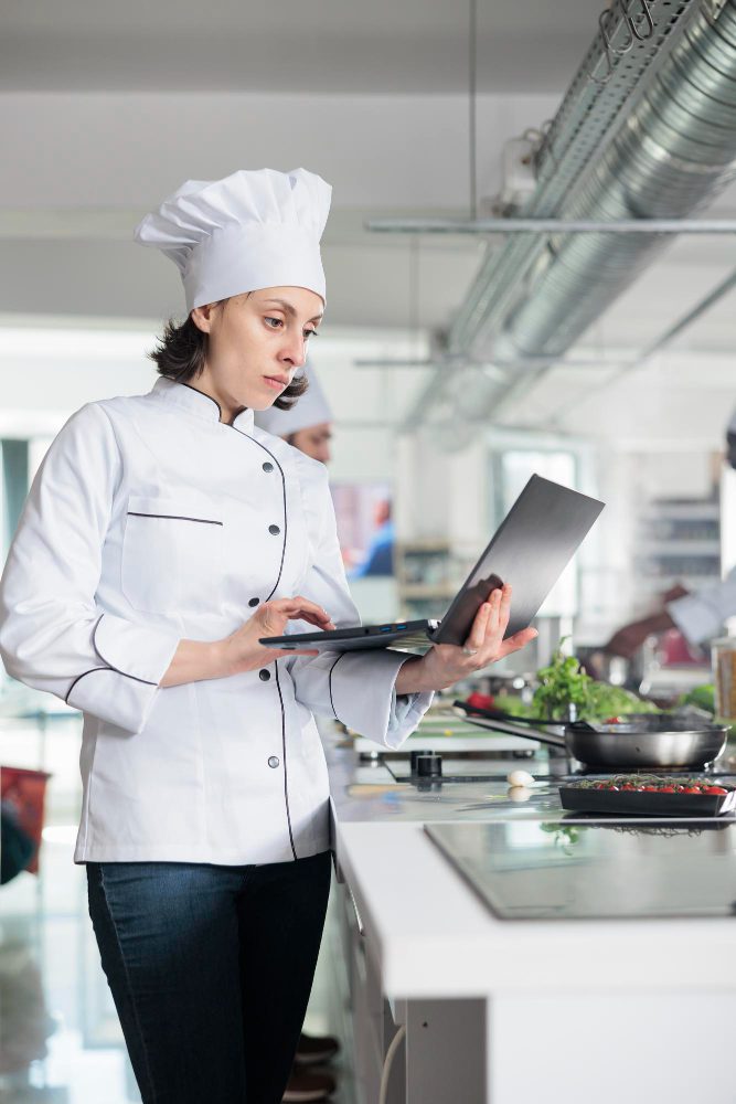 Website design - chef in whites using a laptop in a commercial kitchen