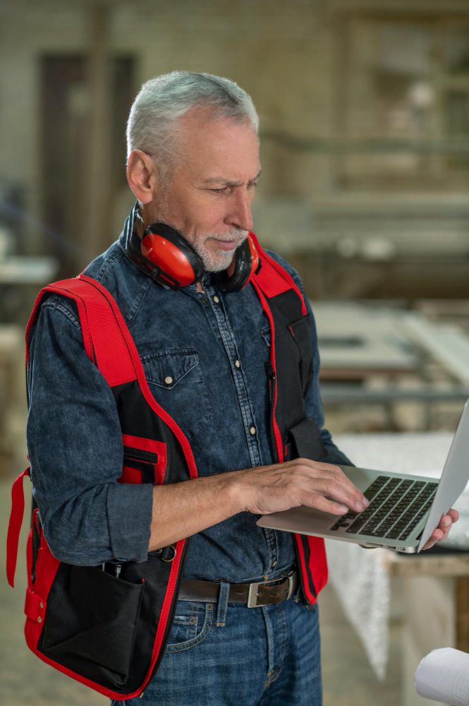 Website design - tradesman in a work vest using a laptop on site