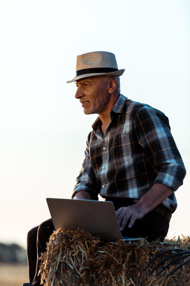 Website design - farmer in a hat using a laptop while sitting on a hay bale