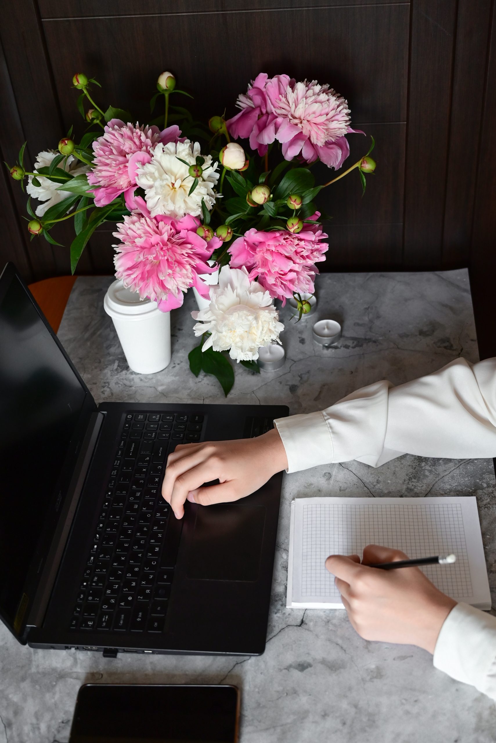 Website design - hands typing on a laptop at a desk with pink peonies