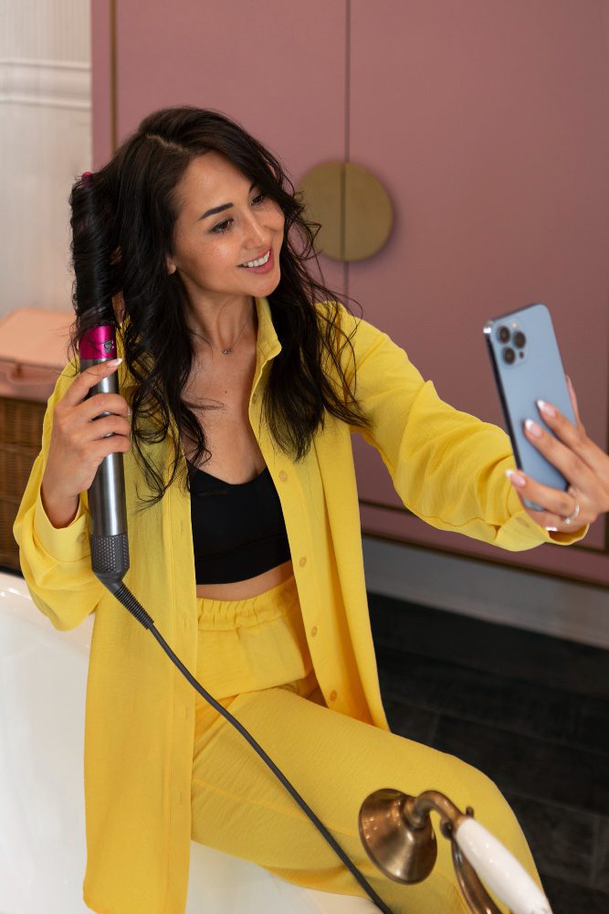 Social media - woman in a yellow suit recording content on her phone