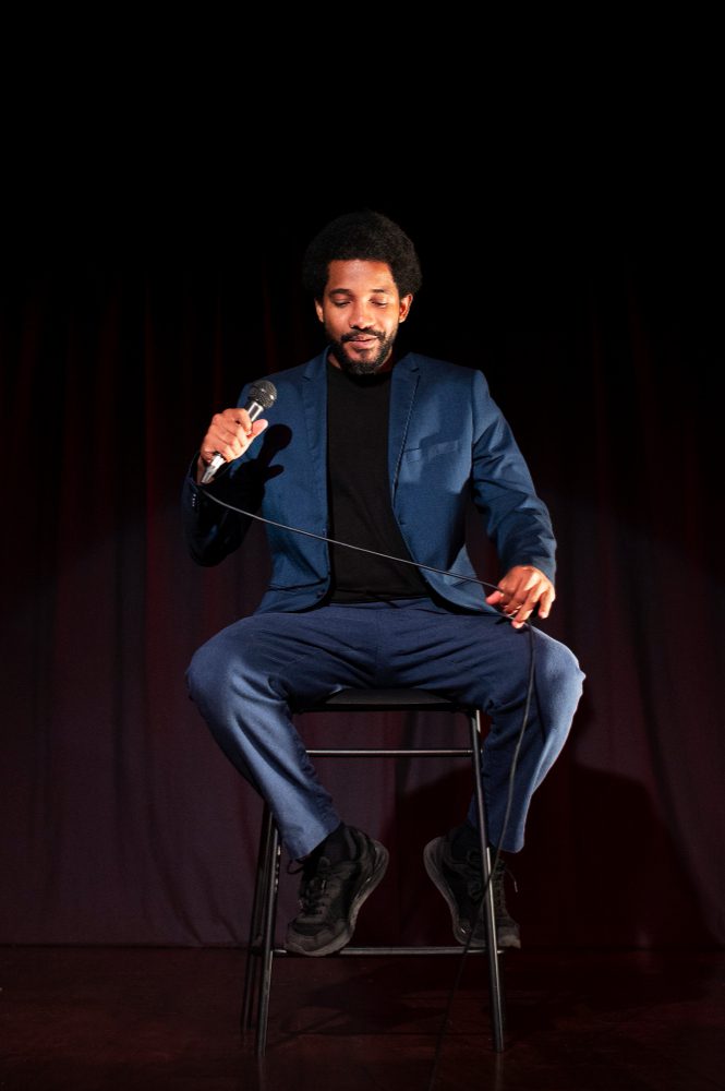 Social media - man sitting on a stool with a microphone on a dark stage