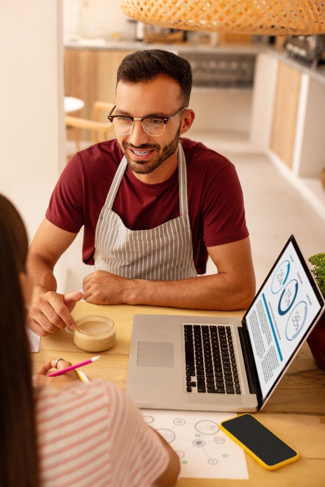 Ecommerce websites - shopkeeper in an apron serving a customer beside a laptop