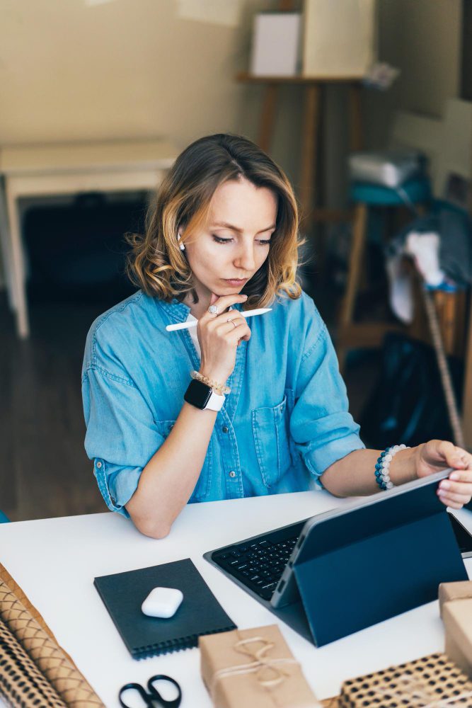 Website design - woman pausing to think at a laptop, stylus in hand