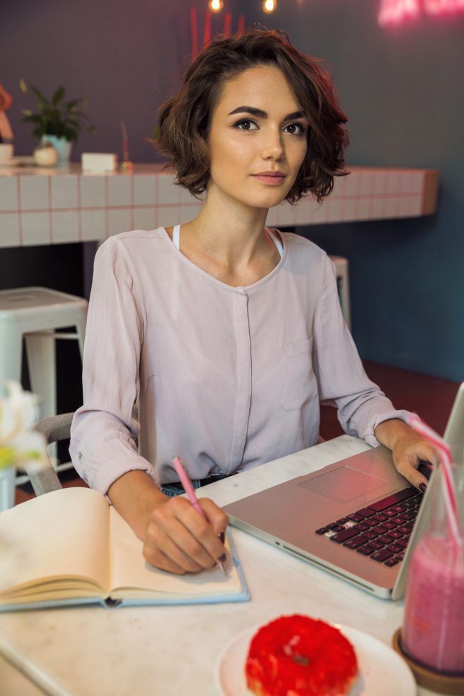 Website design - woman writing in a notebook beside a laptop in a cafe