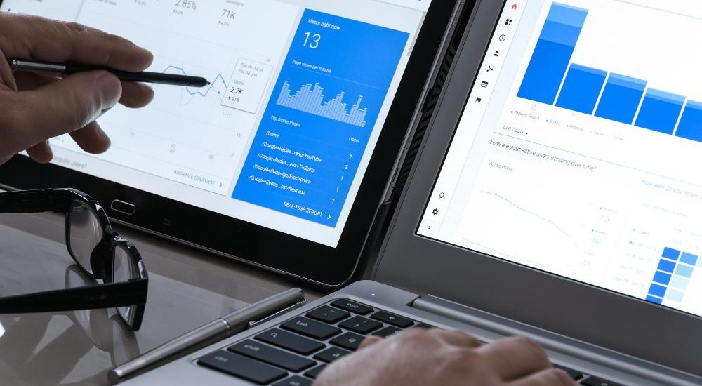 SEO - hand pointing at analytics dashboards on two screens
