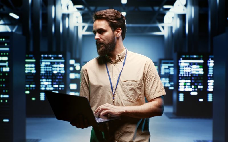 Engineer using laptop to monitor energy consumption across server components and distributors. Expert ensuring data center sensors for temperature and humidity are functioning optimally